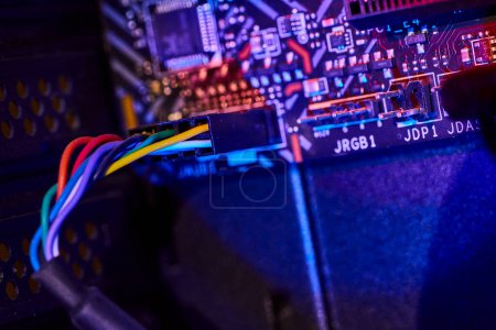 Nahaufnahme der Computermotherboard beleuchtet durch blaue und lila Lichter, präsentiert komplizierte Schaltungen und ein mehrfarbiges Flachbandkabel in Fort Wayne, Indiana.