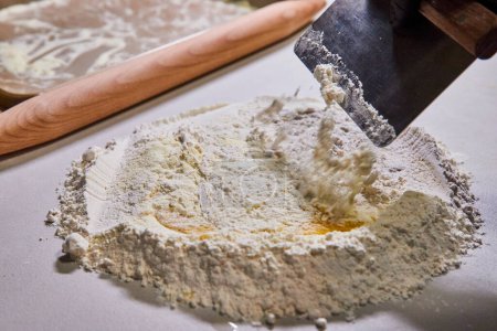 Foto de Hornear artesanal en una cocina de Fort Wayne, capturando la preparación íntima de pasta con harina, huevo y raspador de masa. - Imagen libre de derechos