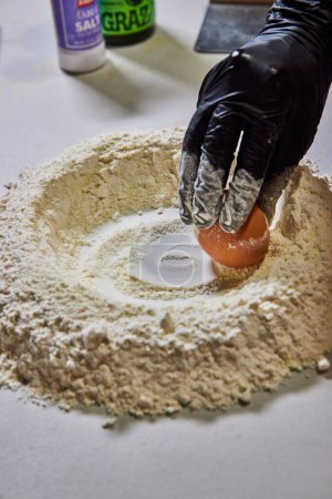 Midwestern culinary tradition showcased in Fort Wayne, Indiana, with close-up of homemade pasta preparation process - cracking an egg into flour well.