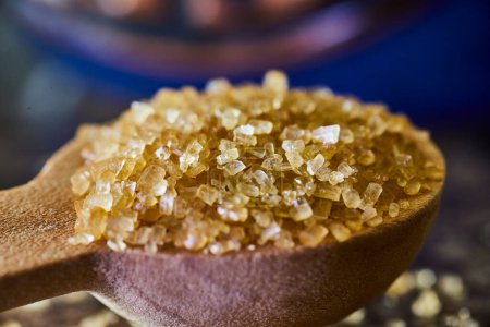 Nahaufnahme natürlicher brauner Zuckerkristalle auf einem Holzlöffel, die in einer sonnigen Küche Indianas an Backatmosphäre erinnert.