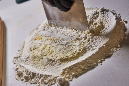 Hand in black glove mixing fresh flour for homemade pasta, capturing the art of culinary preparation in a Fort Wayne kitchen