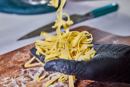 Handmade Tagliolini Pasta in Progress - A Gloved Hand holds Fresh Noodles in a Rustic Kitchen setting, Fort Wayne, Indiana.