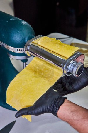 Fresh homemade pasta being rolled in Artisan machine in an American kitchen, emphasizing hygiene with black gloves