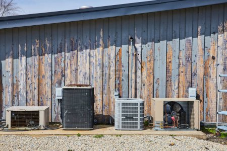 Quatuor d'unités de climatisation vieillissant gracieusement sur un mur rustique de bois d'écurie en Spiceland, Indiana, symbolisant l'utilité et la résilience.