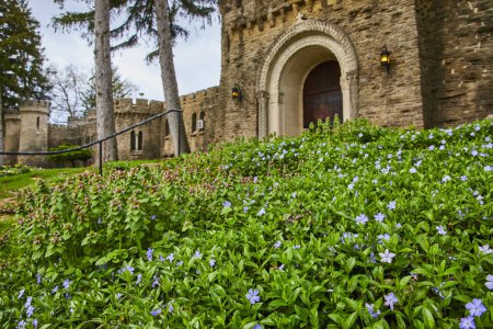 Springtime at Bishop Simon Brute College in Indiana, showcasing a majestic medieval-style castle framed by lush periwinkles and verdant foliage.