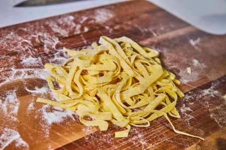 Handgemachte fettuccine Pasta auf einem rustikalen Holzbrett in einer sonnenbeschienenen Küche, die traditionelle italienische Kochkunst aus Indiana präsentiert.
