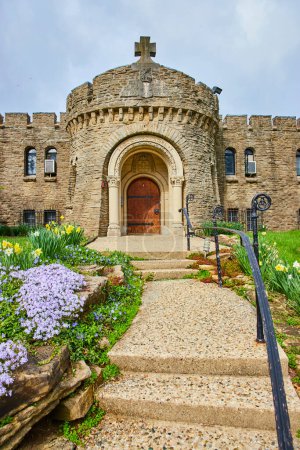 Primavera en el Bishop Simon Brute College, mostrando una acogedora entrada de un castillo de piedra de estilo medieval con vibrantes alrededores florales.