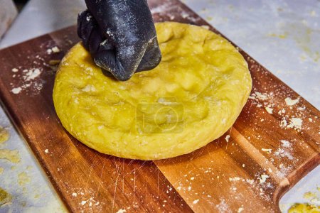 Artisanal Pasta Creation in Indiana - Close-up of gloved hands delicately shaping fresh, yellow pasta dough on a well-used wooden board.