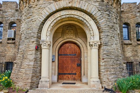 Entrada de piedra ornamentada del Bishop Simon Brute College en Indianápolis, mezclando historia con modernidad, adornada por floraciones de primavera.