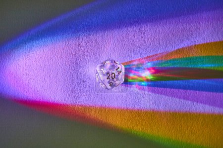 Macro view of a transparent D20 dice casting a vibrant rainbow spectrum on a surface, symbolizing gaming, science, and creativity
