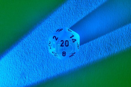 Luminous blue twenty-sided die casting shadow on contrasting green and blue backdrop, symbolizing gaming strategy and the thrill of chance.