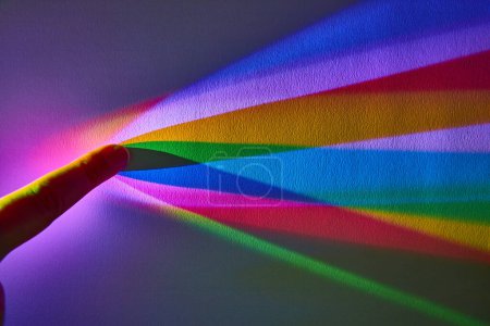 Lebhaftes Spektrum von Regenbogenfarben, unterbrochen durch menschliche Finger, die Interaktion von Licht und Wahrnehmung hervorheben