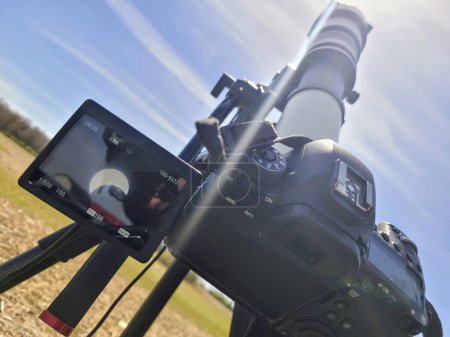 Cámara DSLR profesional en trípode capturando un eclipse en Spiceland, Indiana bajo un cielo azul claro.