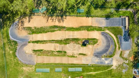 Aerial view of a sunlit BMX track in Warsaw, Indiana, with aligned benches and lush greenery.