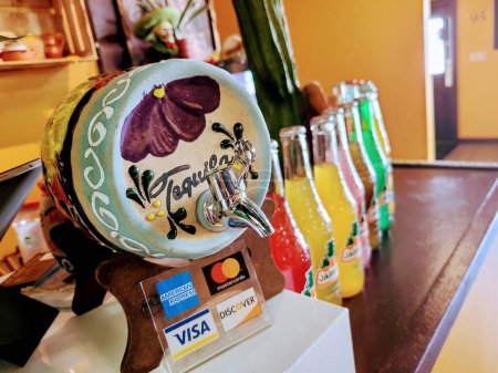 Foto de Dispensador de tequila pintado a mano en un acogedor café Fort Wayne, con opciones de pago modernas y botellas de colores. - Imagen libre de derechos