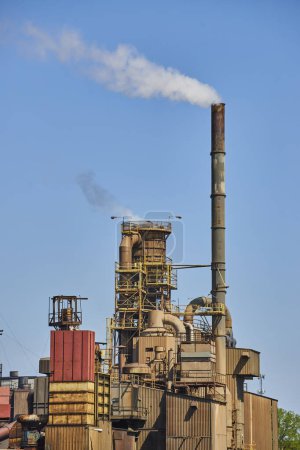 Industrieanlage in Warschau, Indiana, mit einem hoch aufragenden Schornstein, der Rauch gegen einen klaren blauen Himmel abgibt.