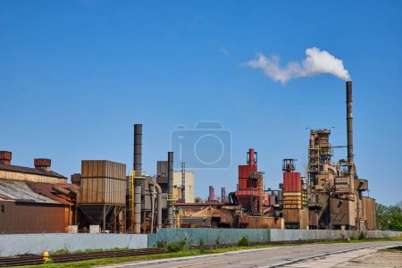 Photo for Industrial powerhouse under vibrant skies, Warsaw, Indiana: expansive factory with smoking chimneys and vivid blue backdrop. - Royalty Free Image