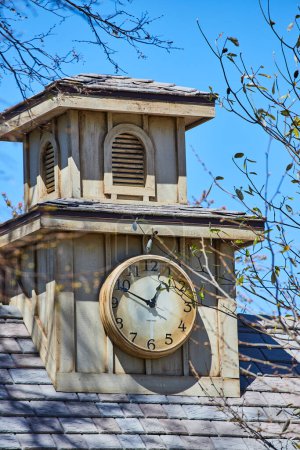 Vintage clock tower at Fort Wayne, framed by spring branches against a blue sky, embodying timeless charm.
