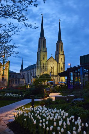 Téléchargez les photos : Twilight embrasse une église historique avec deux flèches à Fort Wayne, face à un jardin de tulipes blanches. - en image libre de droit