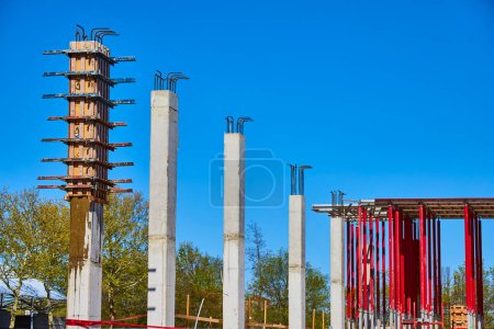Rising concrete pillars dominate a bustling Fort Wayne construction site under a clear blue sky.