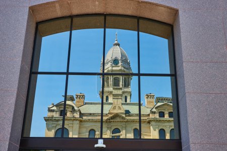 Historic Kosciusko County Courthouse reflects on modern glass facade, blending timeless architecture under clear skies.