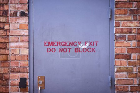 Puerta de salida de emergencia resistida en una pared de ladrillo, Fort Wayne, destacando la seguridad y la decadencia urbana.