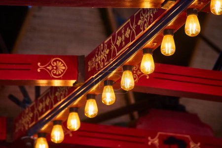 Warme Edison-Glühbirnen leuchten unter einem reichen, rot-goldenen Geländer und verschmelzen Tradition mit Modernität in einem intimen Rahmen.