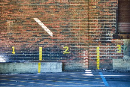 Urbane Präzision: Bemalte Ziffern 1 und 2 kennzeichnen Parkplätze in einem sonnenbeschienenen, in die Jahre gekommenen Backsteingrundstück in der Innenstadt von Fort Wayne.