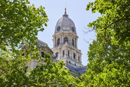 Historic Kosciusko County Courthouse with ornate dome, framed by lush greenery under a clear blue sky.