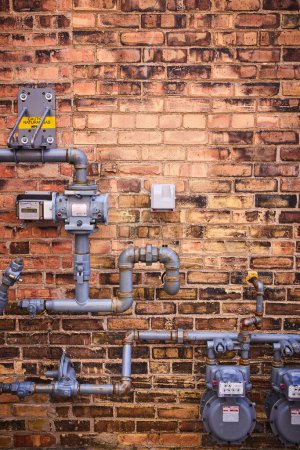 Des compteurs de gaz et des tuyaux complexes sur un mur de briques détérioré, mettant en valeur l'infrastructure urbaine de Fort Wayne.