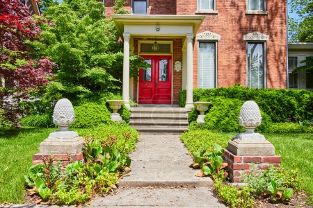 Téléchargez les photos : Journée ensoleillée dans une maison en brique classique à Fort Wayne avec des portes rouges vibrantes et une verdure luxuriante, incarnant chaleur et bienvenue. - en image libre de droit