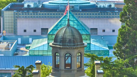 Aerial view of downtown Portland Oregon showcasing the historic Pioneer Courthouse with its elegant dome juxtaposed against a modern glass building adorned with an American flag. Urban harmony of old