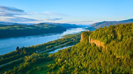 Aerial view of Columbia Gorge in Oregon with the Vista House at Crown Point. Lush forests, a meandering river, and the stunning early morning light create a serene and picturesque landscape.
