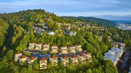 Aerial view of Portland, Oregon at sunrise. Modern townhouse community with red roofs nestled in lush greenery. Quaint homes and tall trees blend urban living with nature, highlighting serene suburban