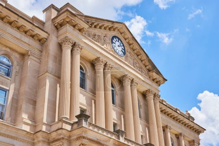 Majestätische Fassade des Huntington County Superior Court in Indiana. Korinthische Säulen und detaillierte Schnitzereien stehen hoch unter einem strahlend blauen Himmel und erinnern an Themen wie Gerechtigkeit, Regierungsführung und Architektur.