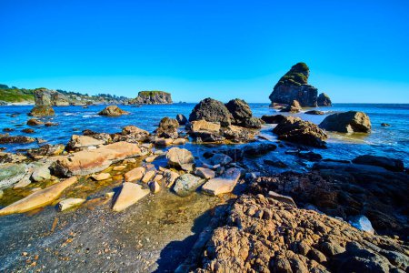 Robuste Küstenlandschaft im Harris Beach State Park, Oregon. Verwitterte Felsen und hoch aufragende Formationen verschmelzen mit dem ruhigen Meer unter einem klaren blauen Himmel. Ideal für Reisen, Natur und Umwelt