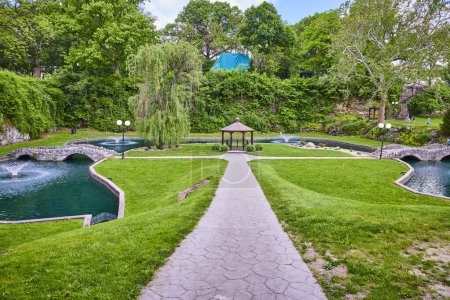Stroll through Huntington Indianas Sunken Gardens featuring a charming stone bridge picturesque gazebo and vibrant fountain. Perfect for community events or peaceful relaxation amidst lush greenery