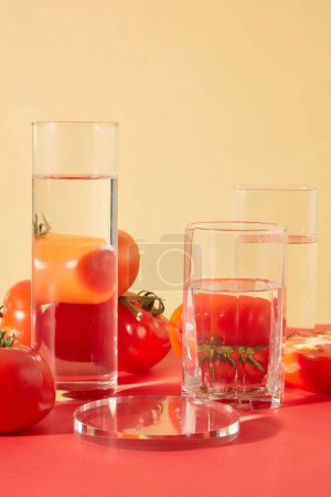 Téléchargez les photos : Gros plan des verres d'eau transparents affichés sur la table avec des tomates rouges juteuses. Les tomates contiennent des composés qui aident à rétrécir les pores, traiter l'acné, apaiser les coups de soleil et éclaircir le teint de la peau. - en image libre de droit