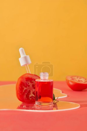 Téléchargez les photos : Bouteille de sérum placée à côté d'une tomate coupée en deux sur une feuille acrylique transparente. Mettre l'accent sur le concept des cosmétiques faits maison avec des ingrédients naturels et respectueux de la peau. - en image libre de droit