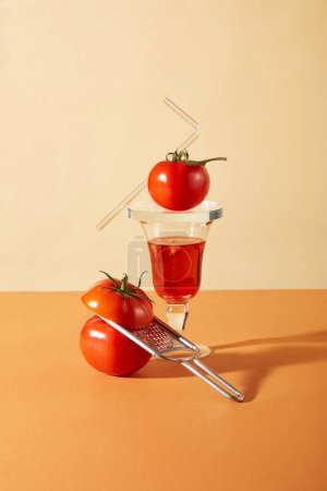 Foto de Un vaso de jugo de tomate, tomates frescos y un rallador arreglado sobre un fondo. Beba un vaso de jugo de tomate todos los días para complementar sustancias antiinflamatorias como carotenoides y riboflavina.. - Imagen libre de derechos