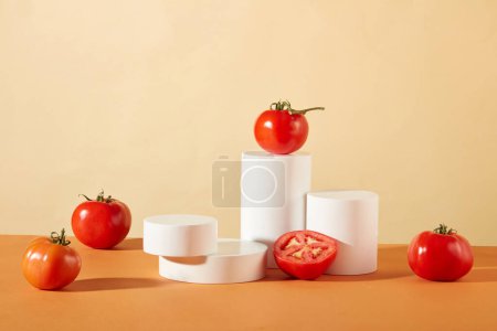 Téléchargez les photos : Tomates fraîches et podiums blancs présentés sur fond orange-beige. Grand espace pour l'affichage des produits, incarnant le concept de cosmétiques végétaliens. - en image libre de droit