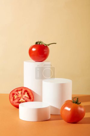 Foto de Vista frontal de tomates frescos y plataformas blancas que se muestran sobre un fondo naranja y beige. Espacio para la visualización del producto. Concepto de cosmética vegana. - Imagen libre de derechos