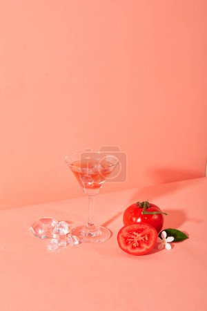 Téléchargez les photos : Tomates fraîches affichées avec un verre à cocktail sur un fond rose. Les tomates sont une excellente source de vitamines A et C qui aident à prévenir la cécité nocturne et à augmenter la vision oculaire.. - en image libre de droit