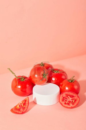 Foto de Los jugosos tomates rojos se colocan alrededor de una plataforma redonda sobre un fondo rosa. Espacio ideal para mostrar cosméticos naturales con extracto de tomate. Primer plano. - Imagen libre de derechos