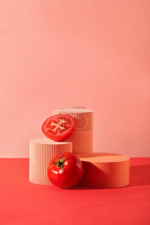 Téléchargez les photos : Tomates fraîches et plates-formes colorées sont placées côte à côte sur un fond rose. Espace créatif pour l'affichage des produits. Les tomates sont très bonnes pour les personnes atteintes de maladies cardiovasculaires et Alzheimer. - en image libre de droit