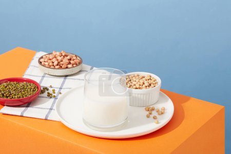 Téléchargez les photos : Le soja, les arachides et les haricots verts sont contenus dans des plats et un bol. Coupe en verre remplie de lait de noix. Différents types de noix peuvent avoir des micronutriments légèrement différents - en image libre de droit