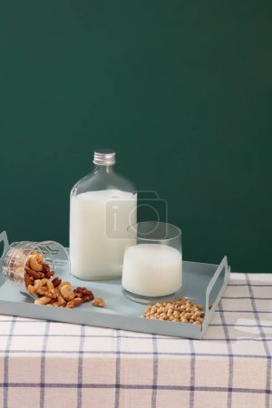 Téléchargez les photos : Bouteille de lait sans étiquette affichée sur un plateau avec une tasse de lait et différents types de haricots et de noix. Modèle pour maquiller votre conception de produits biologiques - en image libre de droit