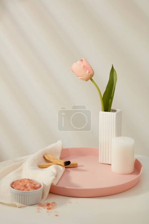 Foto de Una maceta con flor de tulipán expuesta en bandeja con una vela y palo santo humo de madera. Tazón de cerámica de sal himalaya rosa sobre toalla blanca. Espacio en blanco para la promoción de productos de belleza - Imagen libre de derechos
