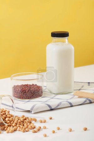 Téléchargez les photos : Bouteille de lait frais avec étiquette vide placée sur un tissu à côté d'un bol de haricots rouges. Beaucoup de soja sont exposés. Les haricots sont riches en fibres bénéfiques fournit de nombreux avantages pour la santé - en image libre de droit
