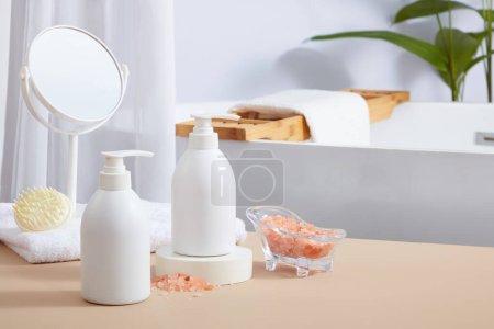 Photo for Front view of unbranded pump bottles displayed in the bathroom with scalp massage brush and a mirror placed on towel. Pink himalayan salt has anti-bacterial and anti-inflammatory properties - Royalty Free Image